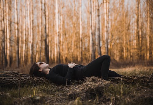 Женщина, лежащая на земле в окружении голых деревьев