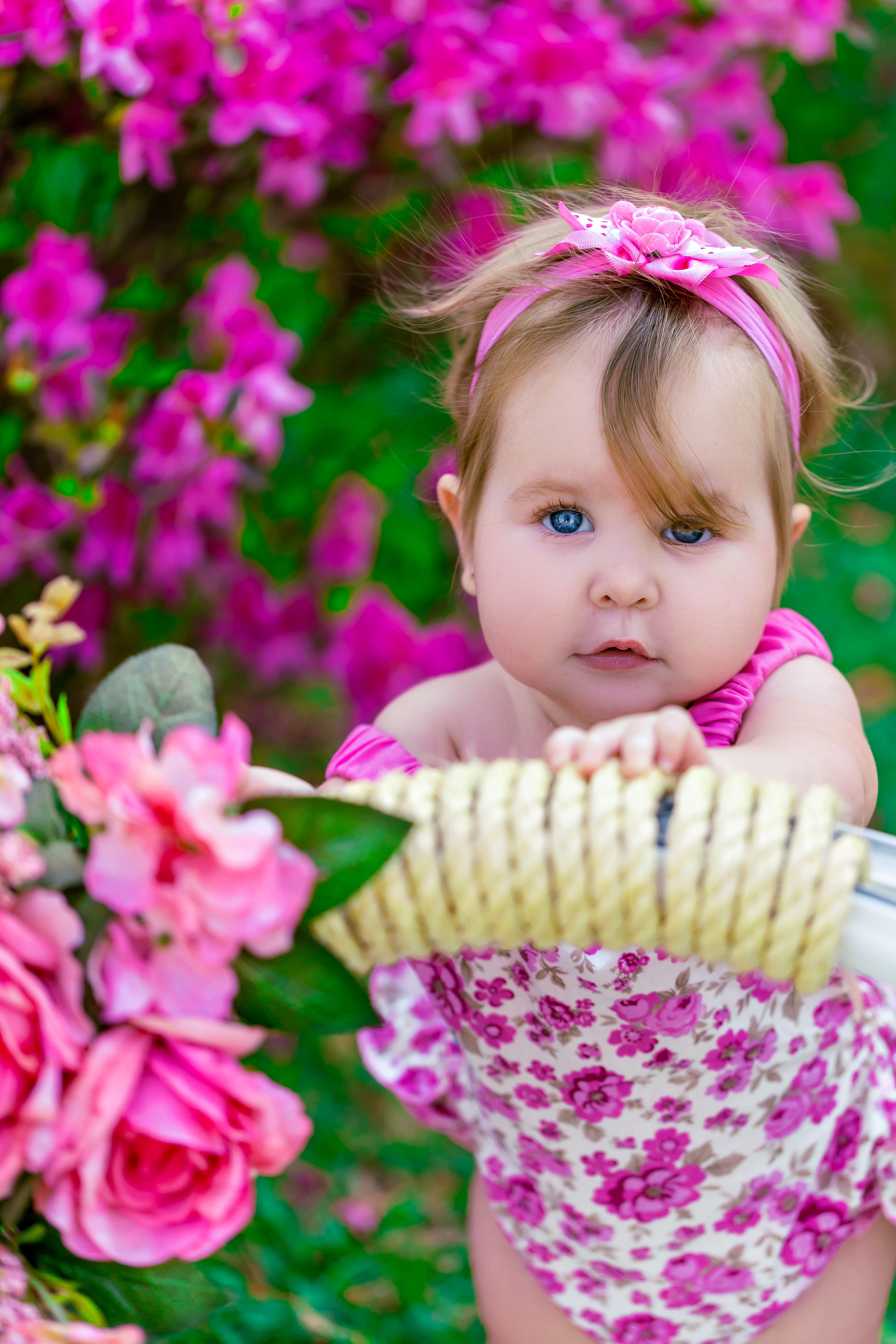 Charming baby girl in floral swimsuit surrounded by vibrant pink flowers, capturing a beautiful spring moment.
