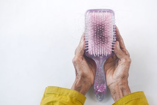 Close-up of senior hands holding a hairbrush with hair strands against a white backdrop.
