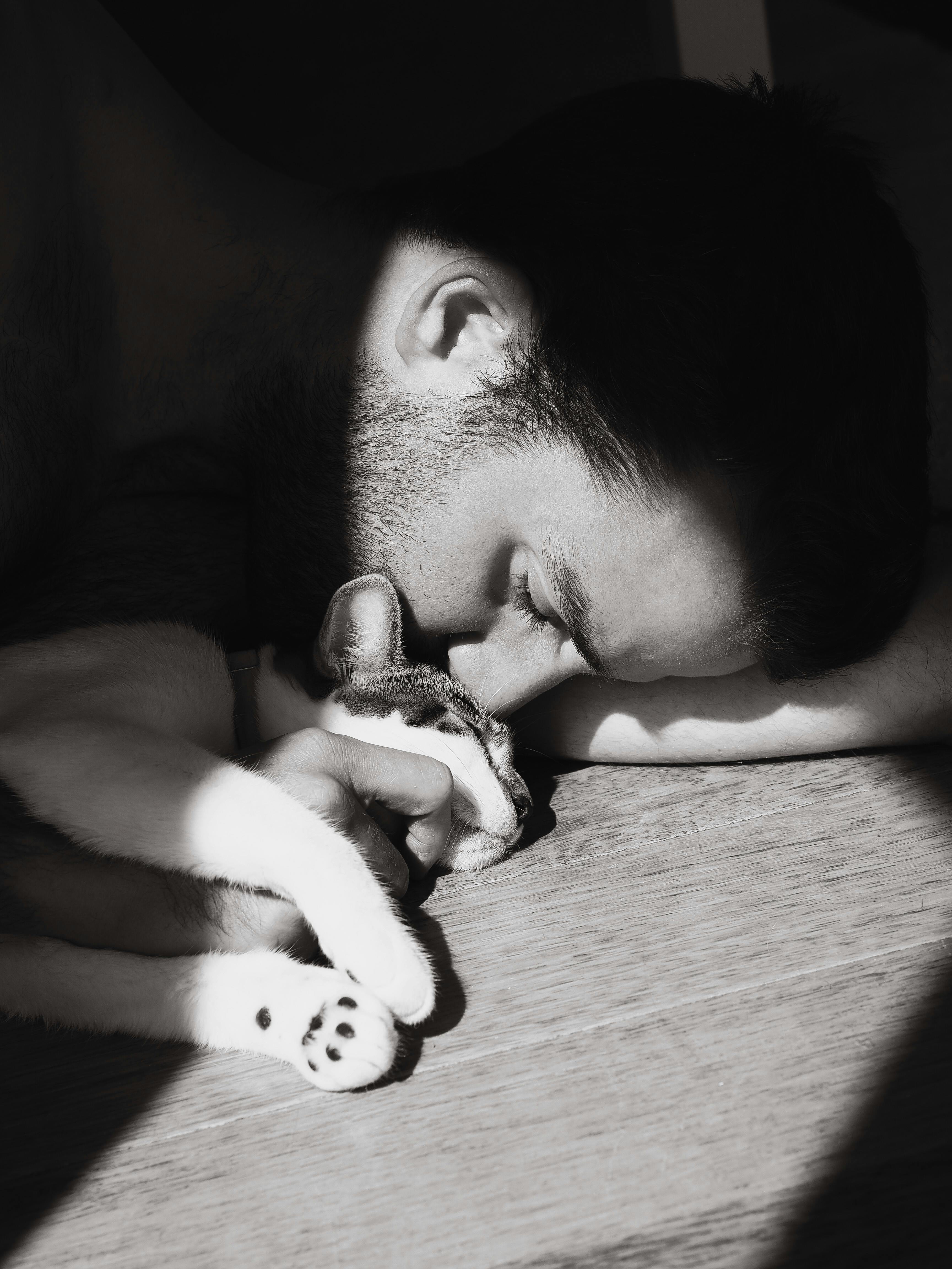 Black and white photo of a man tenderly embracing a sleeping cat, showcasing a peaceful bond of companionship.