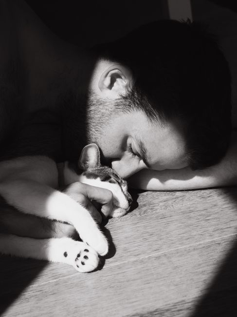 Black and white photo of a man tenderly embracing a sleeping cat, showcasing a peaceful bond of companionship.