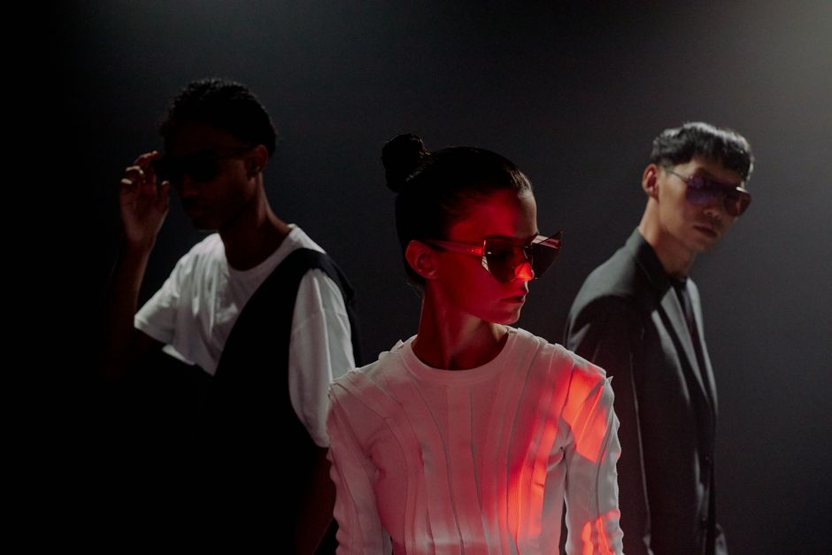 Three models in a studio setting showcasing futuristic fashion and sunglasses.