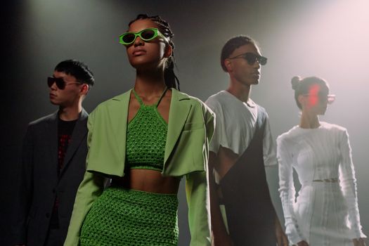 Group of stylish adults in a studio showcasing futuristic fashion under dramatic lighting.