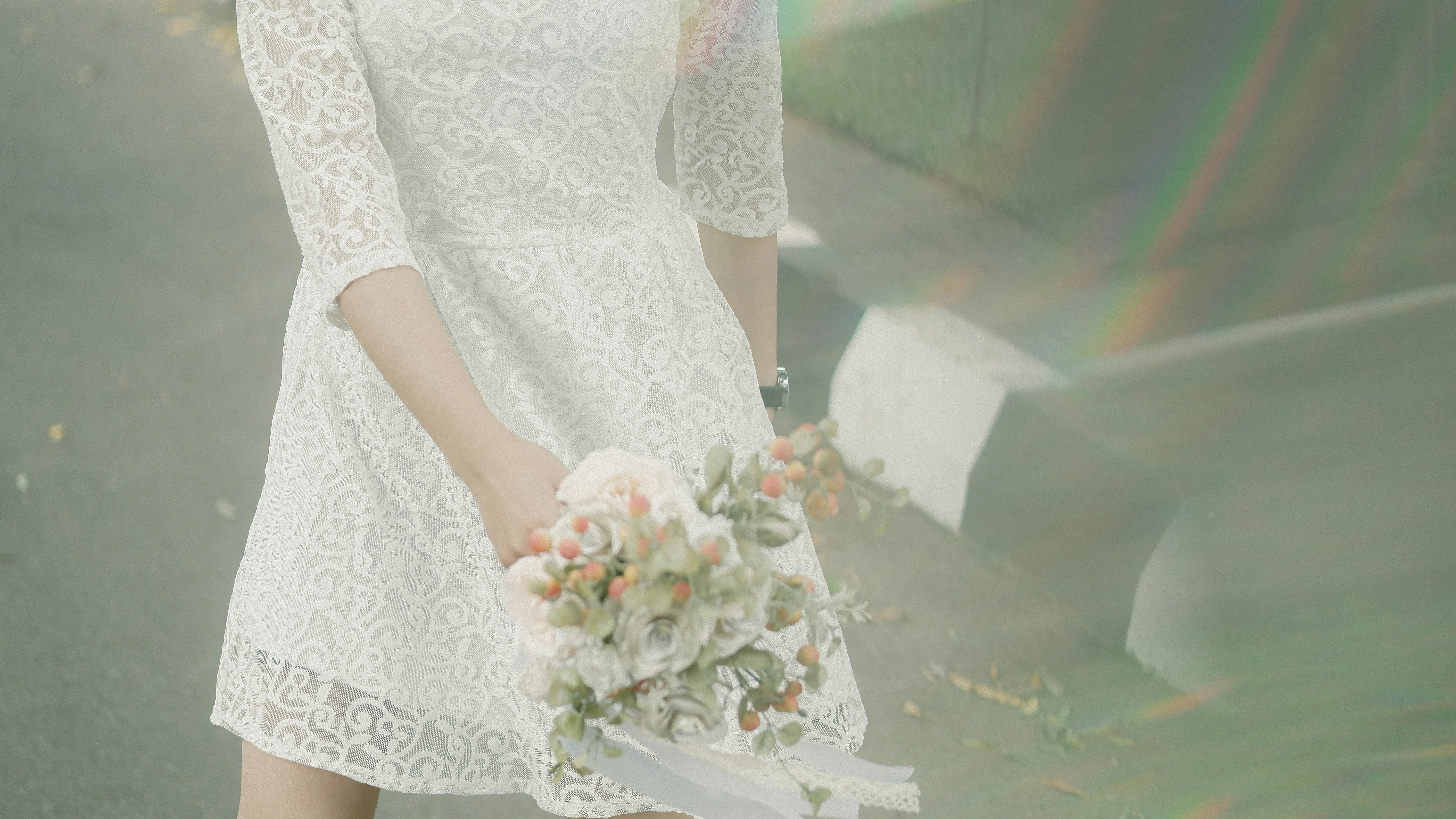 A woman in a white lace dress holding a beautifully arranged bridal bouquet.