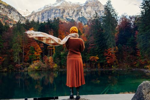 Free A serene autumn landscape with a woman overlooking a tranquil mountain lake surrounded by vibrant foliage. Stock Photo