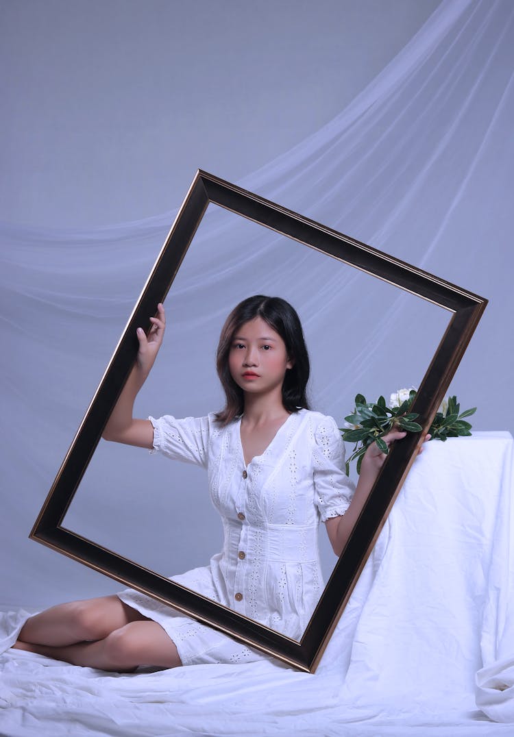 A Girl In White Dress Holding Brown Wooden Frame