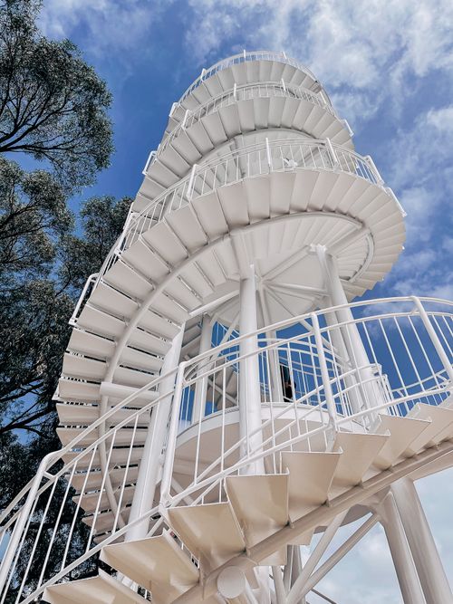 Free Elegant white spiral staircase reaching upwards against a vibrant blue sky. Stock Photo