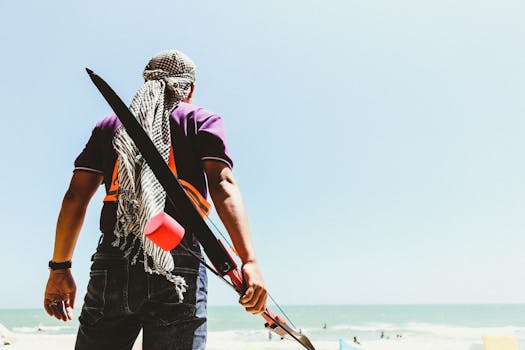Person standing on a beach with a bow, enjoying a bright summer day by the ocean.