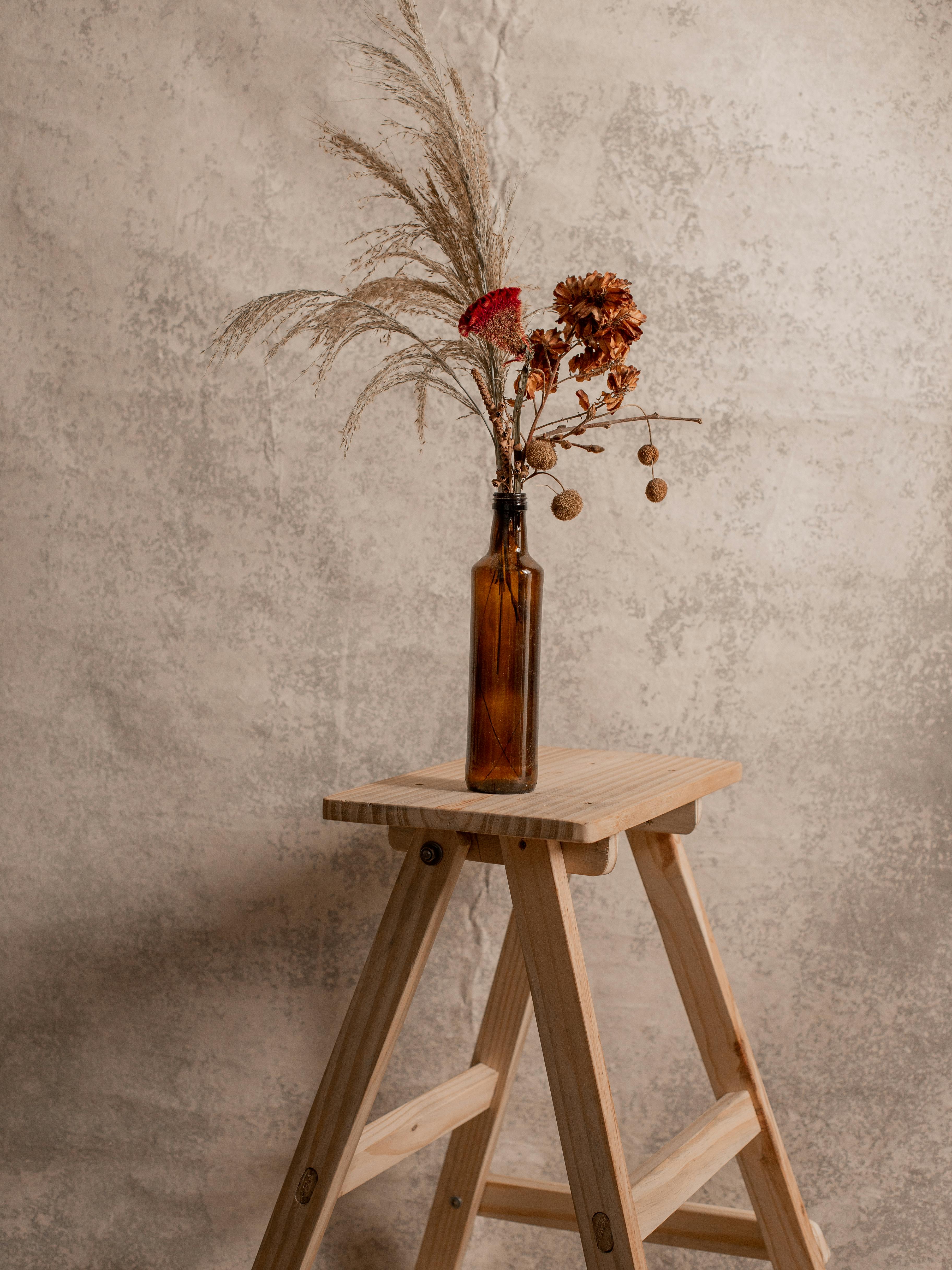 Elegant dried flowers in a bottle on a wooden stool against a rustic concrete background.