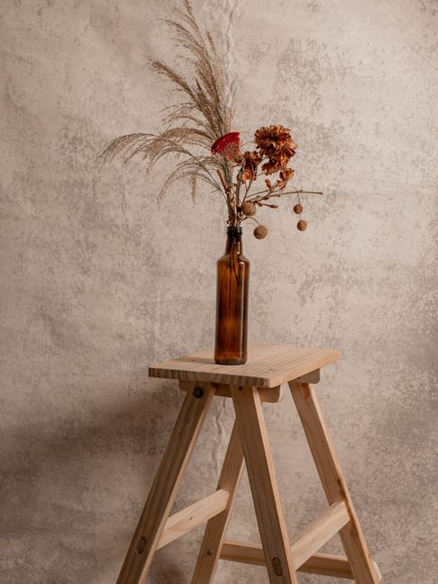 Elegant dried flowers in a bottle on a wooden stool against a rustic concrete background.