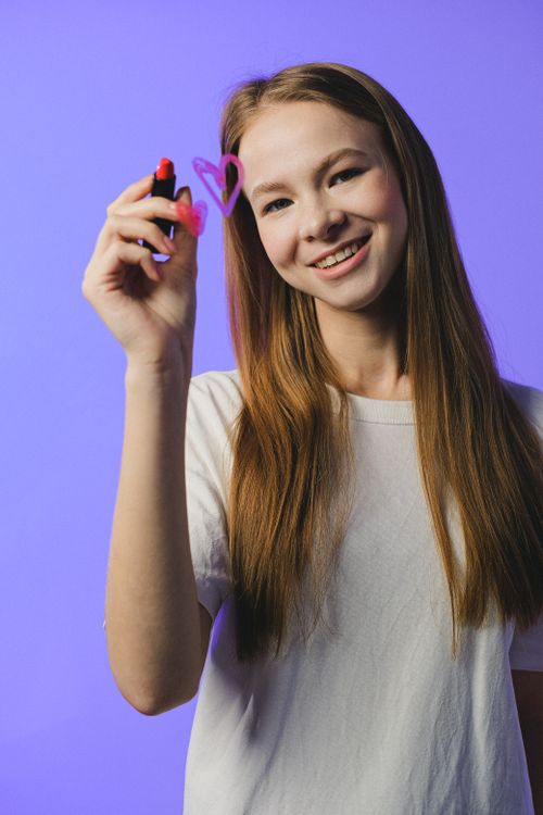 Free Smiling teenage girl with long brown hair draws a heart on a blue background. Stock Photo