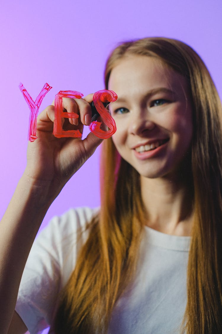 Smiling Teenage Girl Writing Yes On Glass