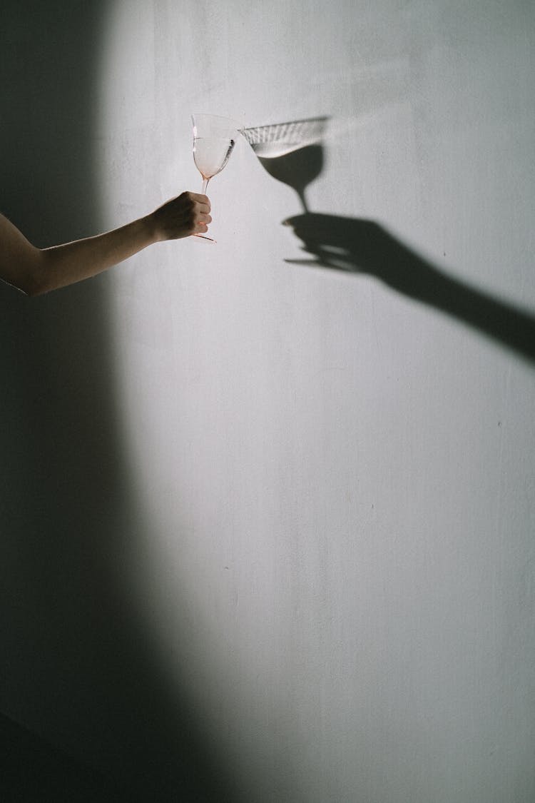 Shadow Of Hand Holding Glass On White Wall