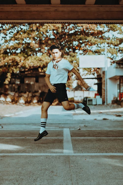 A Man in White Shirt and Black Shoes Jumping on the Street