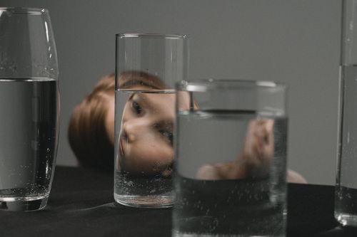 Free Artistic portrait of a woman’s reflection through drinking glasses on a table. Stock Photo