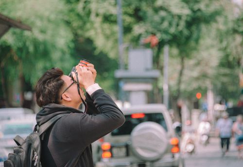 Free A young man uses a camera to capture a vibrant urban street scene during the day. Stock Photo