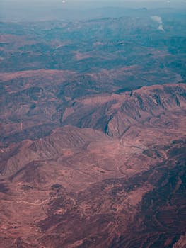 A stunning aerial photograph capturing the expansive barren desert landscape with rugged mountains and clear skies.
