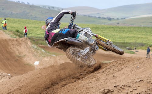 Man in Blue and Black Motocross Suit Riding Motocross Dirt Bike on Brown Dirt Road during