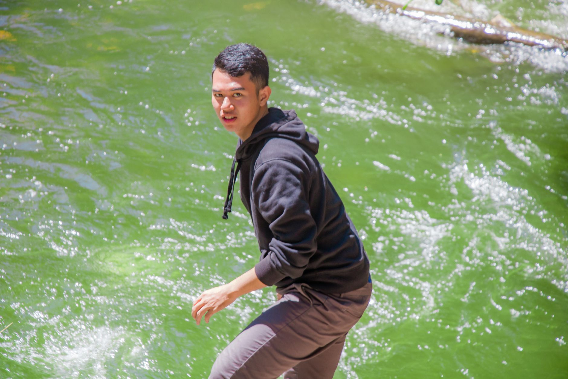 midlife energy crash men over 50 — An Asian man enjoying a brisk day by a scenic river, wearing a hoodie and casual outfit.