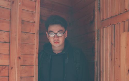 Free A young man wearing glasses stands in a wooden doorway, captured in natural daylight. Stock Photo