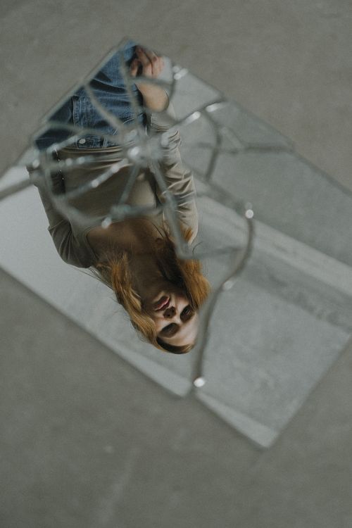 Free Artistic reflection of a woman with red hair in a broken mirror on a gray background. Stock Photo