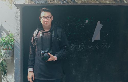 Free Young Asian man with a camera standing outdoors, showcasing street photography style. Stock Photo