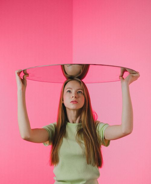 Free Artistic photo of a woman holding a mirror against a pink background. Stock Photo