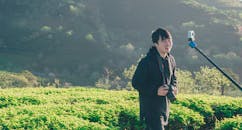 一位摄影师面带微笑，手拿相机，坐在宁静乡村的郁郁葱葱绿色田野中