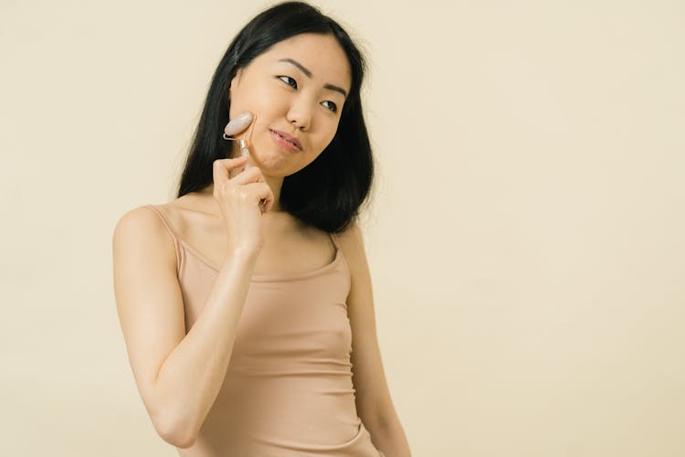 An Asian Woman Smiling And Using gua sha roller 