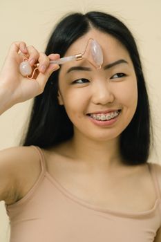 Young woman with long black hair using a gua sha roller for skincare indoors.