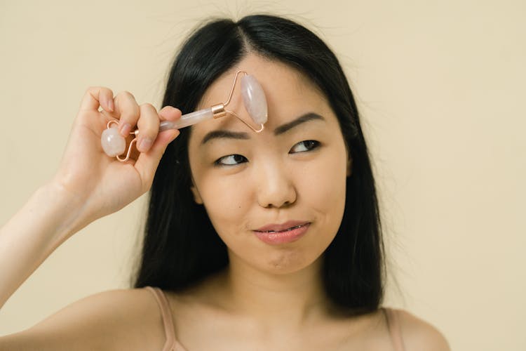 An Asian Woman Holding A gua sha roller On Her Forehead