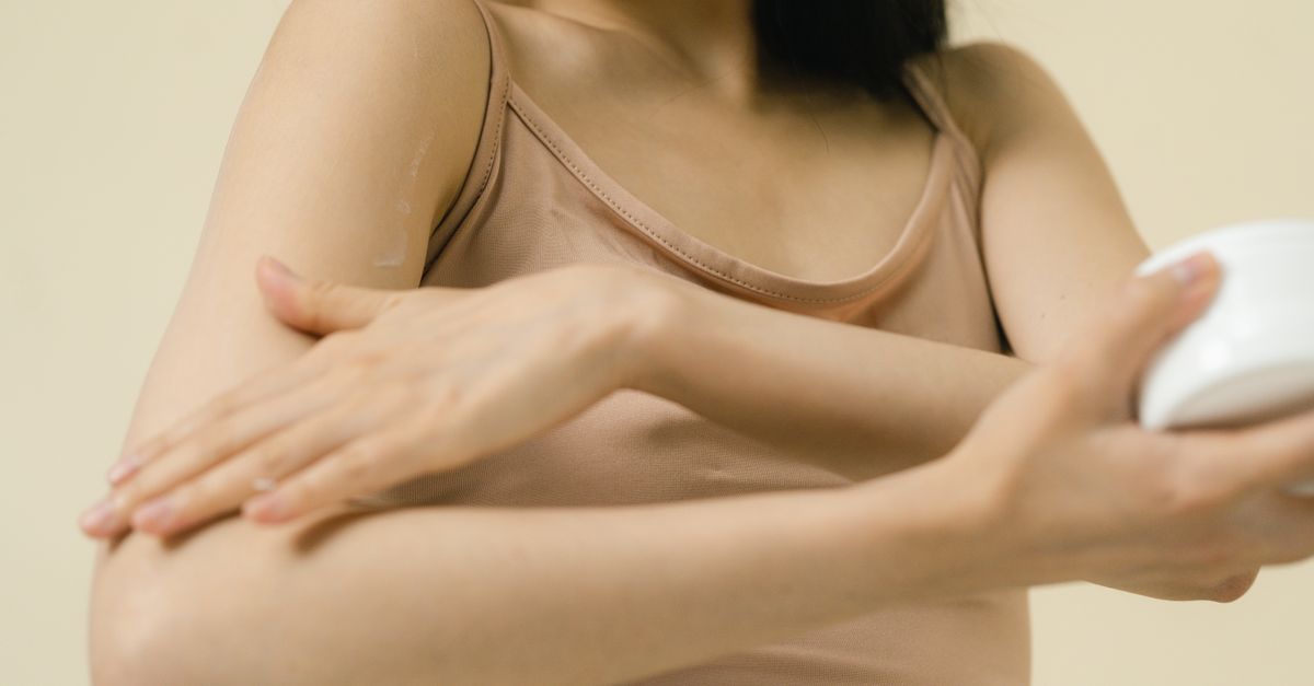 Close-up of a woman applying moisturizer to her arm in a studio setting.