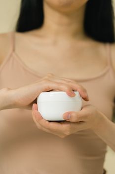 Close-up of a woman holding a white cream jar, focused on skin care and beauty.