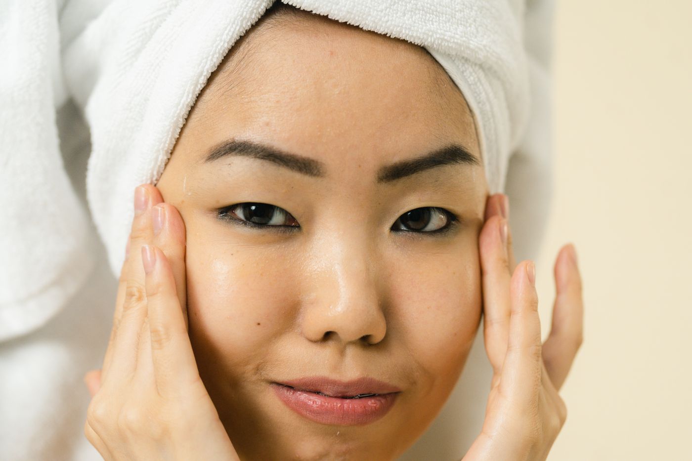 A serene woman wrapped in a white towel turban after a facial, softly lit.
