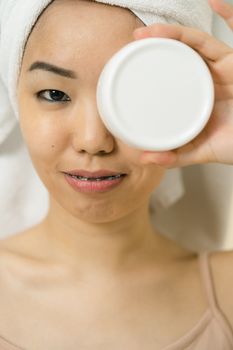 Close-up of a woman in a towel holding a cosmetic jar, focusing on skincare and beauty.