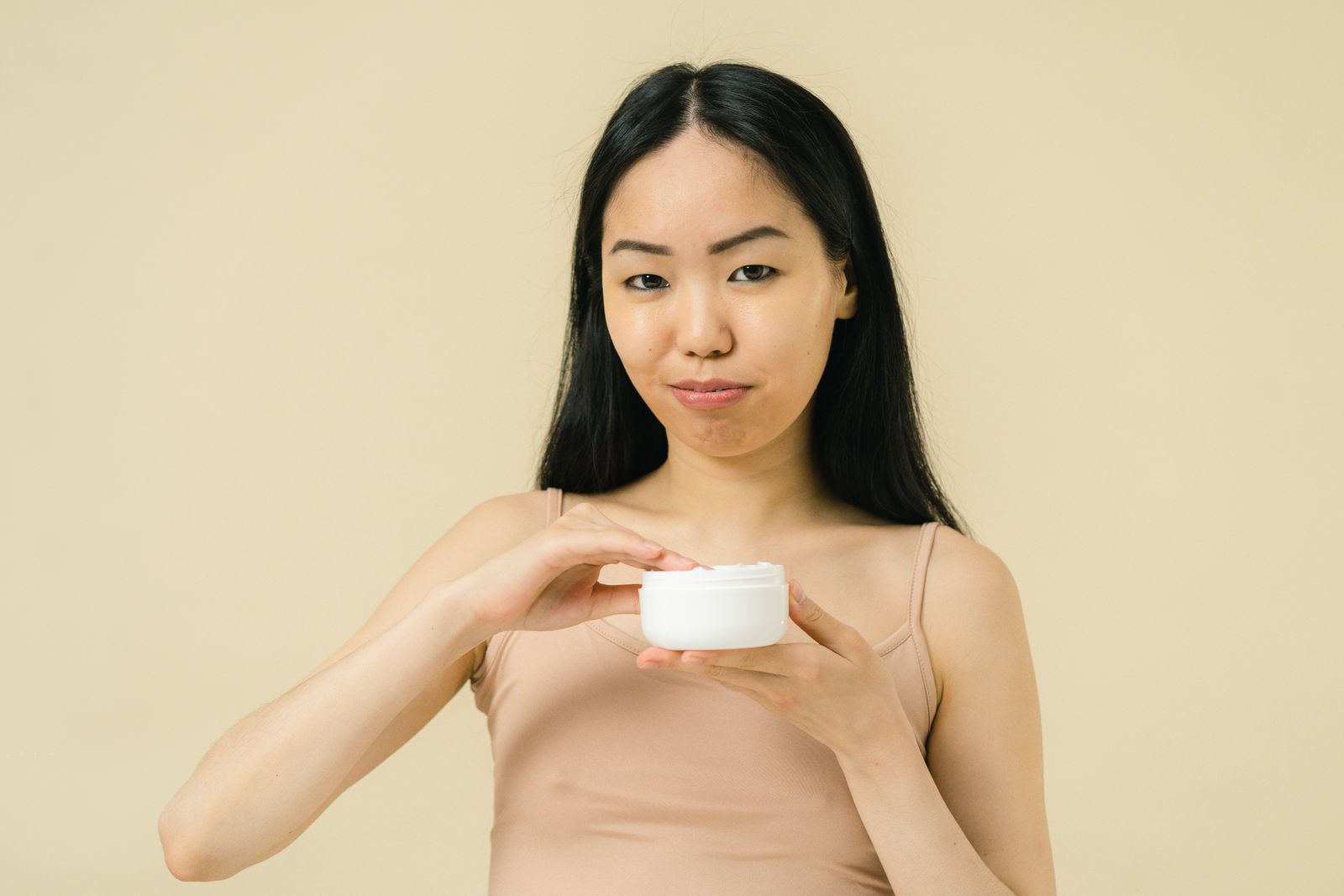 Chica de pelo largo y negro sujetando un tarro de crema facial