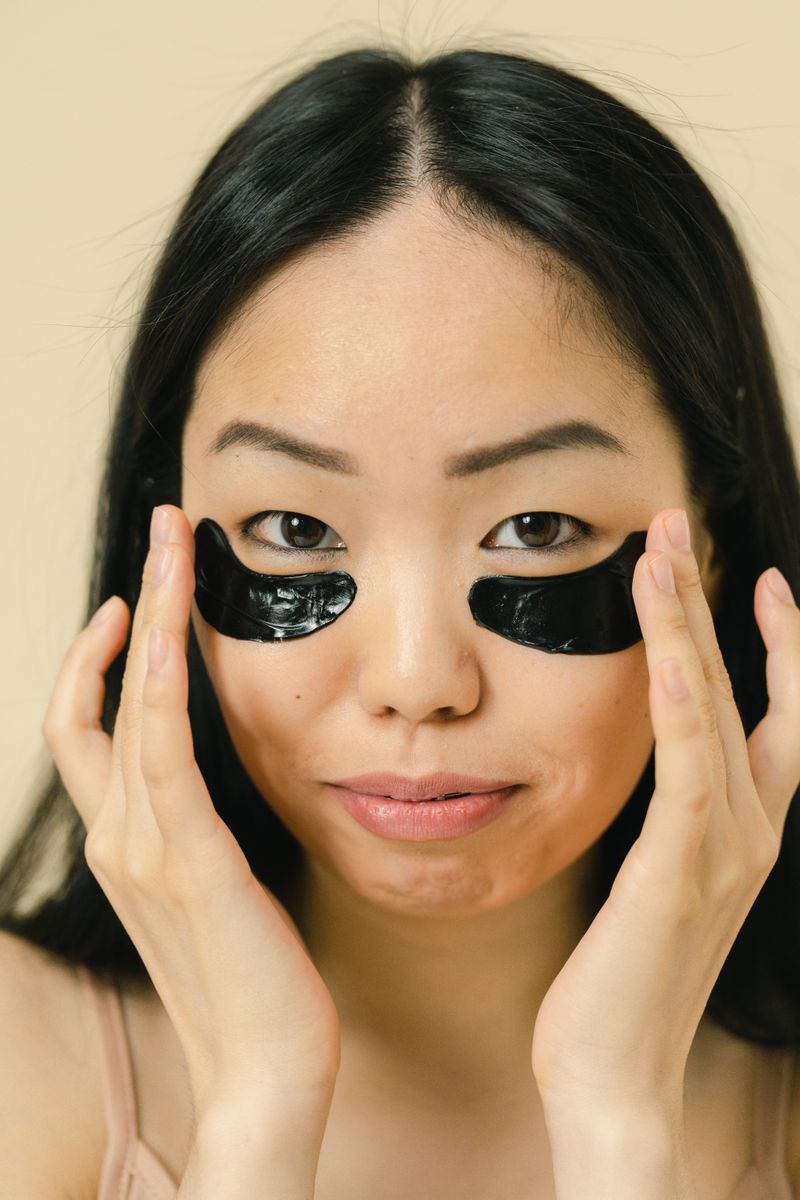 Close-up portrait of a woman applying black eye patches for skincare and self-care routine.
