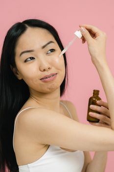 Portrait of an adult woman applying skincare serum, showcasing beauty routine indoors.