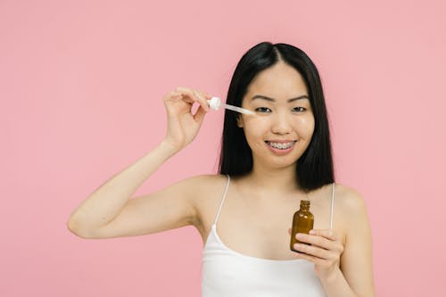 Woman in tank top applying cosmetic product under her eye