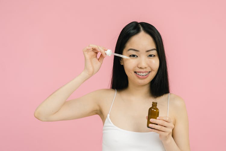 Woman In Tank Top Applying Cosmetic Product Under Her Eye