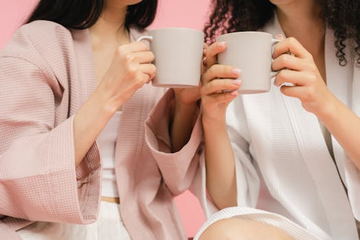 Two women in robes enjoy a coffee break together indoors.