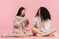 Two women in bathrobes sitting on floor and having break with cup of tea