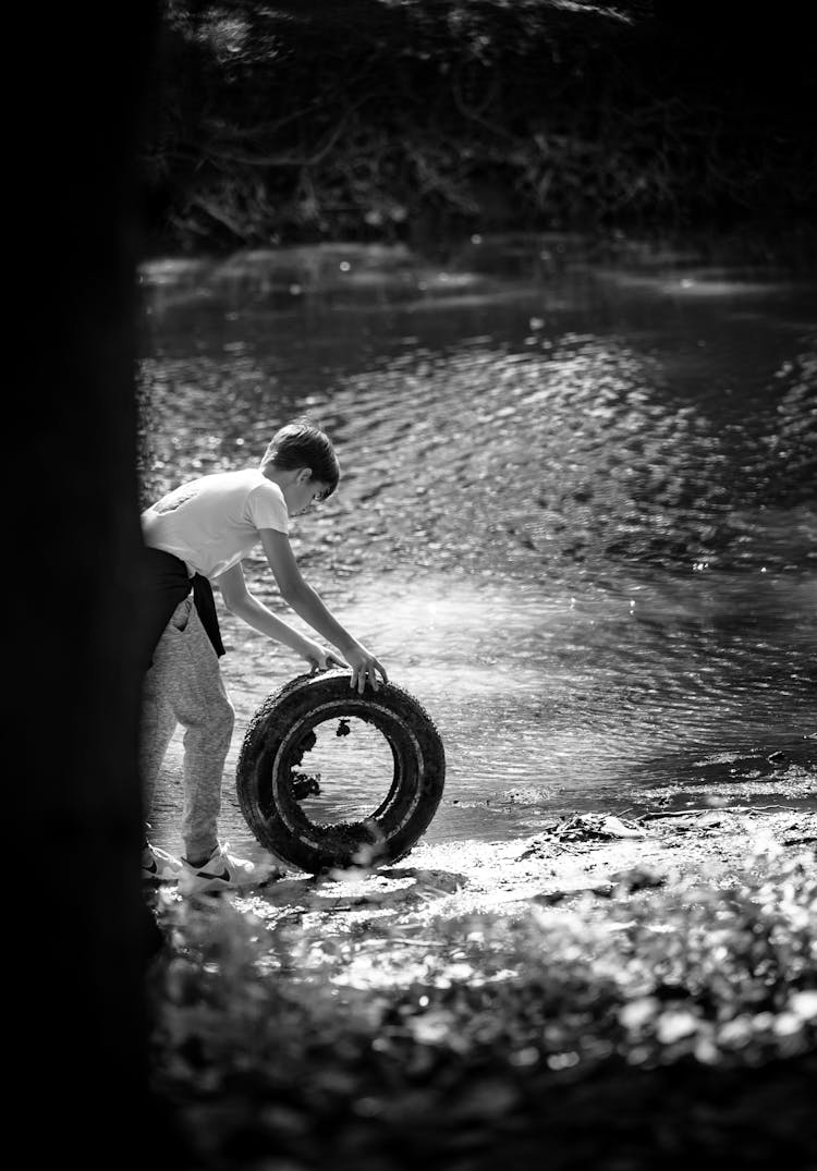 Boy Rolling Old Tyre At Lake Shore