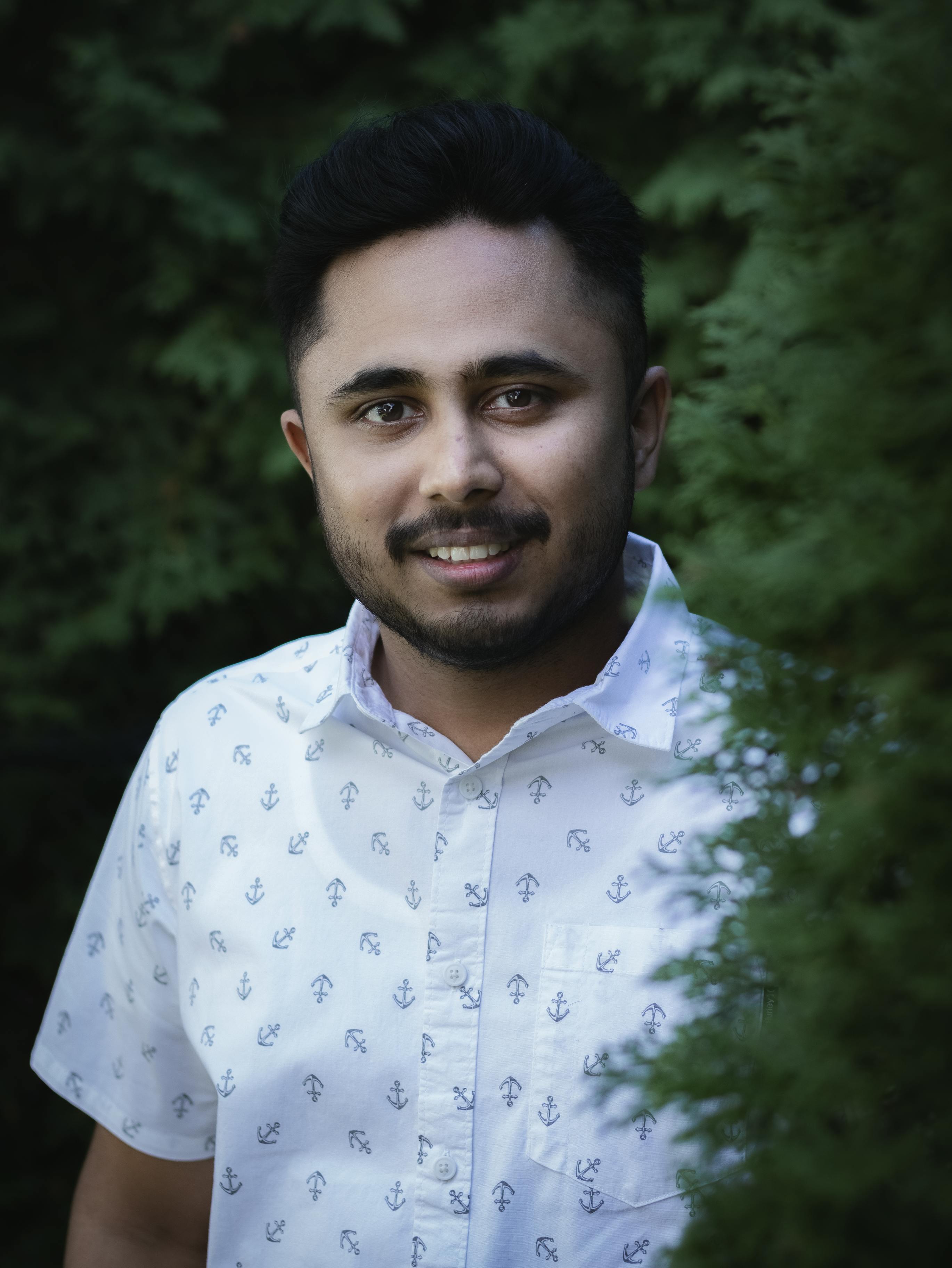 Portrait of a smiling man outdoors wearing a white anchor-patterned shirt in a lush green setting.