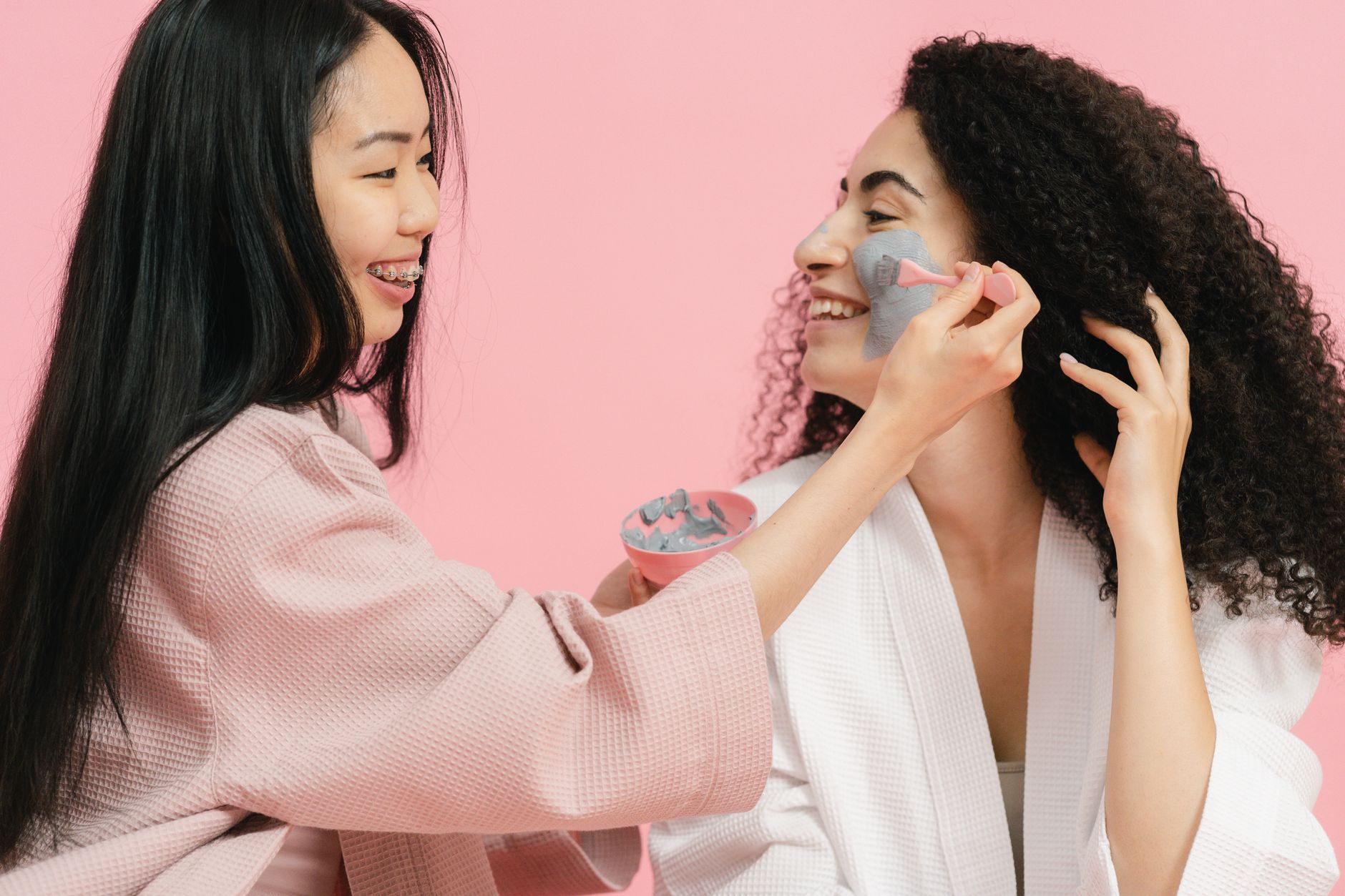 Two women having fun applying face masks and enjoying a skincare routine together.