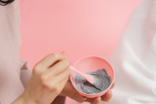 Womans hand mixing gray cosmetic clay in pink bowl