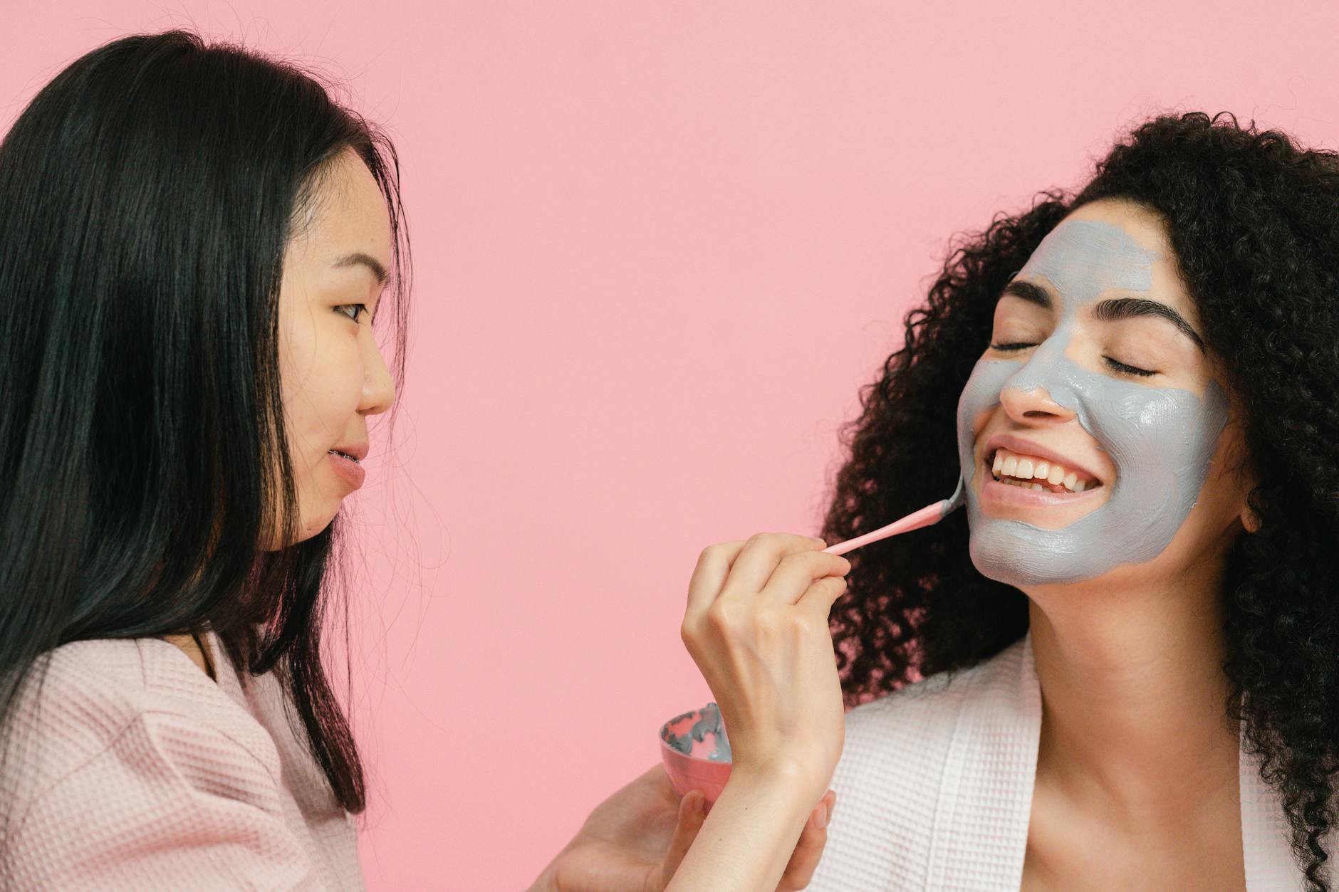 Woman putting on cosmetic mask on face of other woman