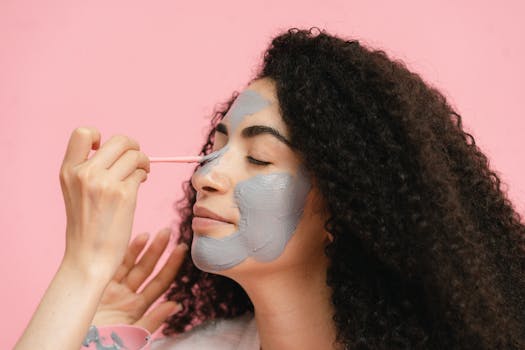 A woman with curly hair applies a gray clay mask, promoting self-care and skincare.