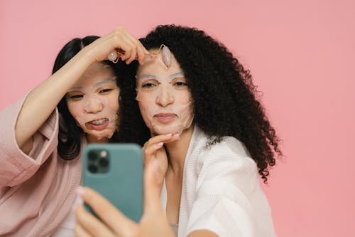 Two women in robes with cosmetic face masks on taking selfie