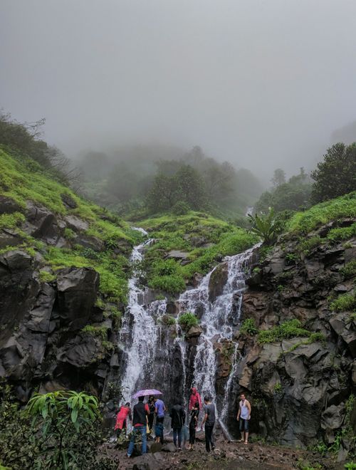 Free A group of people exploring a waterfall in a misty, rocky environment. Perfect for nature and adventure themes. Stock Photo